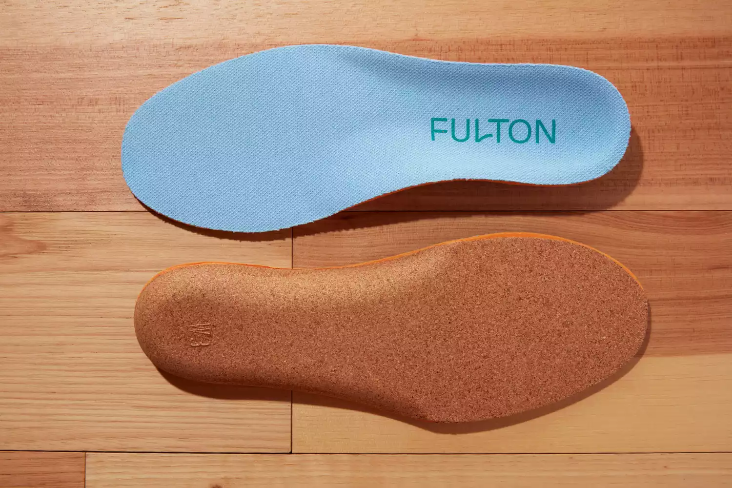 Top and bottom of Fulton Athletic Insoles displayed on a wood floor