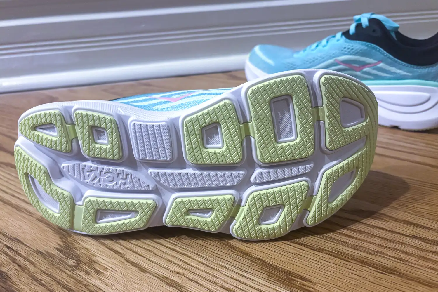 Closeup of the sole design of a running shoe resting on a wooden floor another shoe partially visible in the background