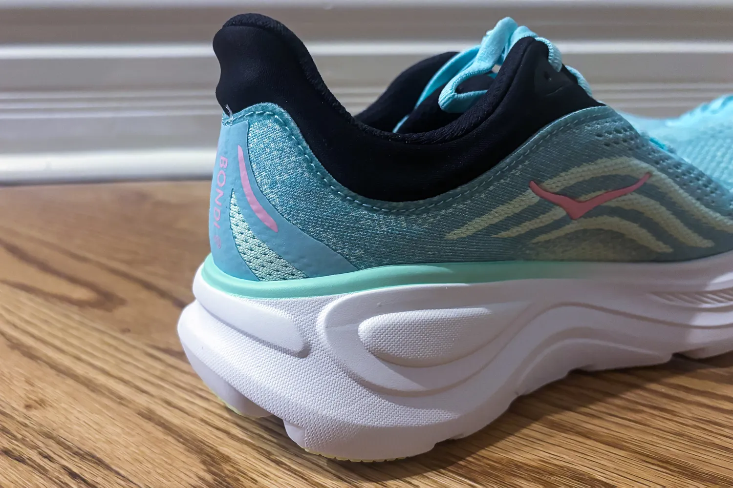 Closeup of the rear part of a running shoe showing the brands details and design features on a wooden floor