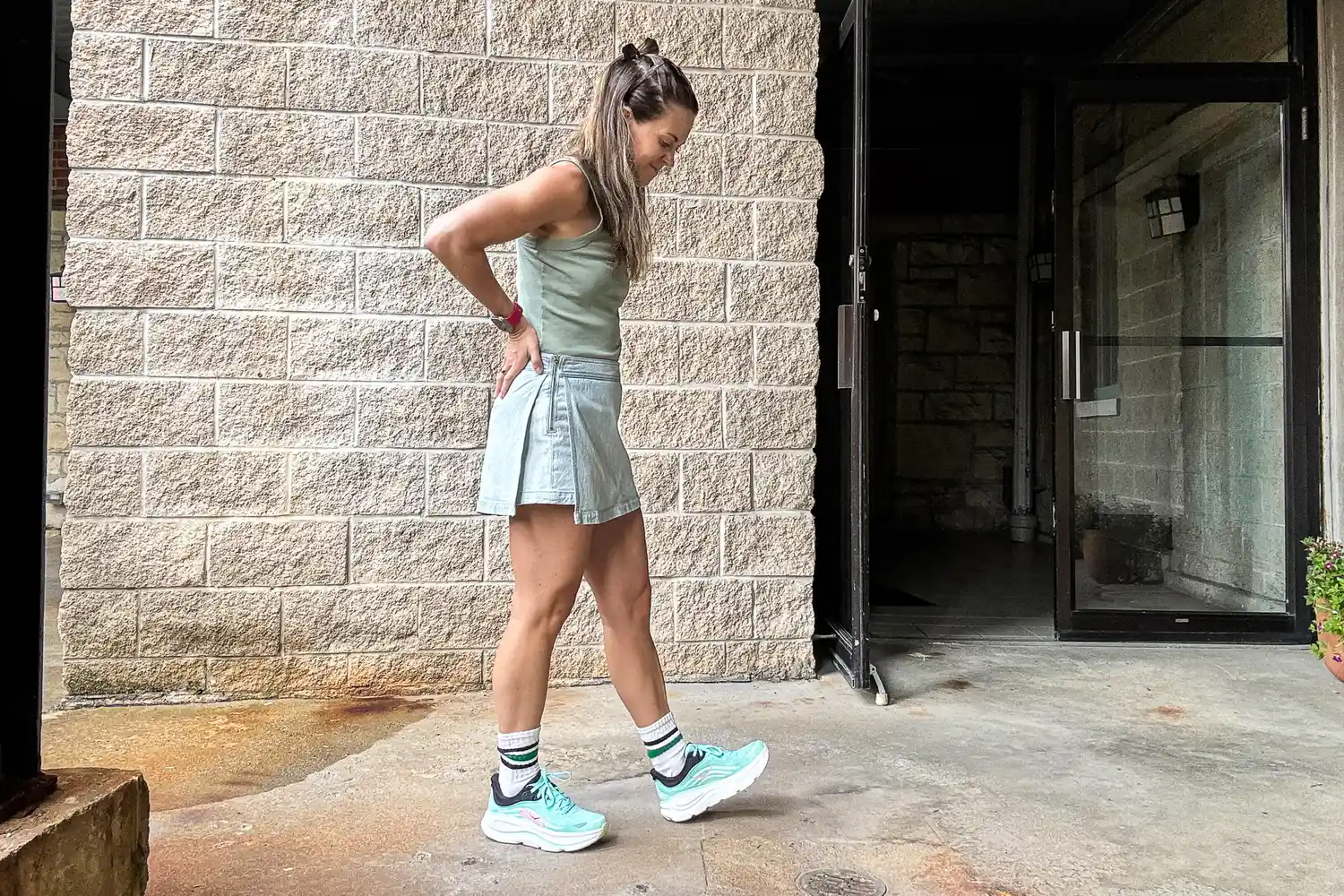 Person standing outside a building next to a brick wall wearing a casual outfit and sneakers