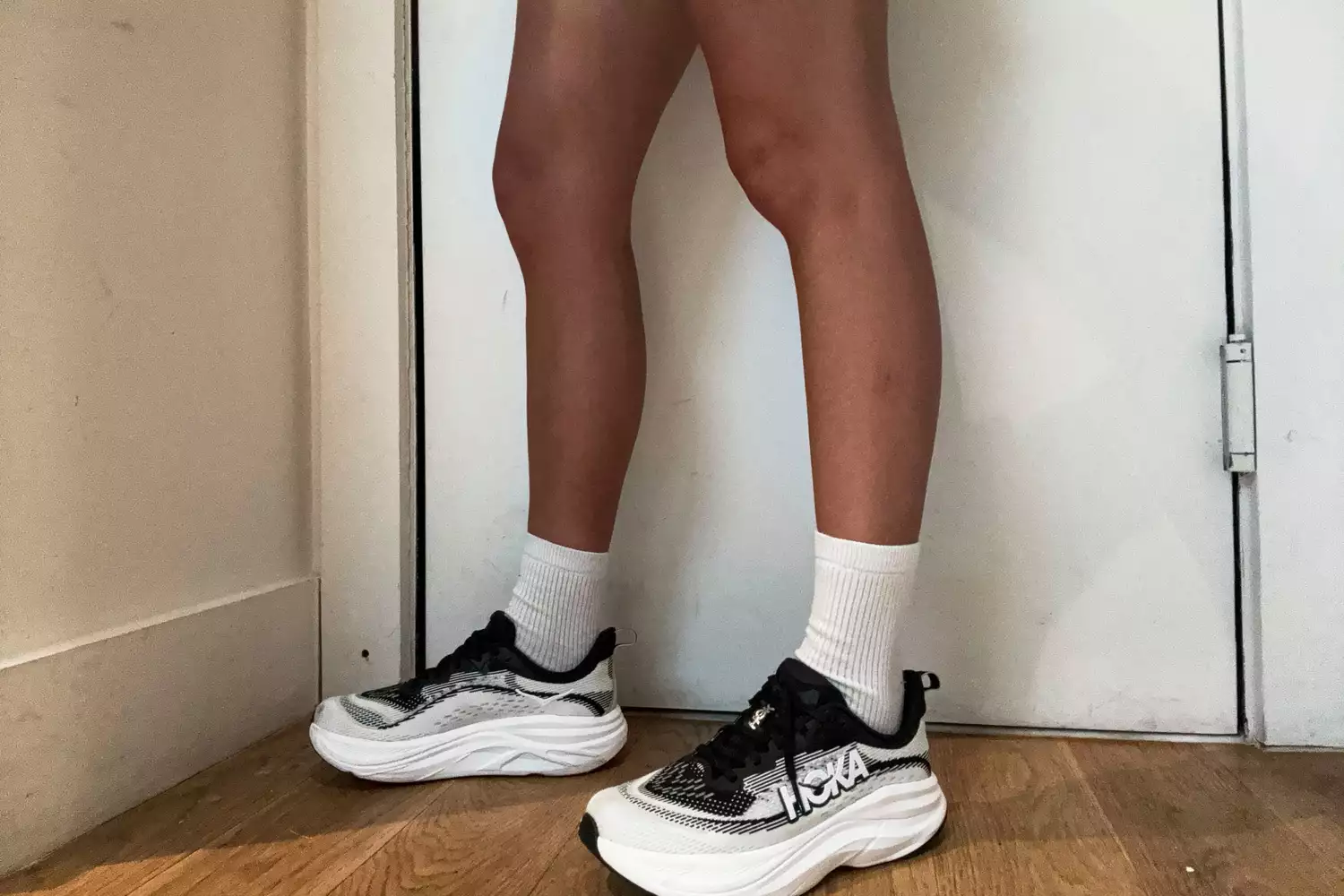 A person stands inside while wearing the HOKA Women's Skyflow Running Shoes