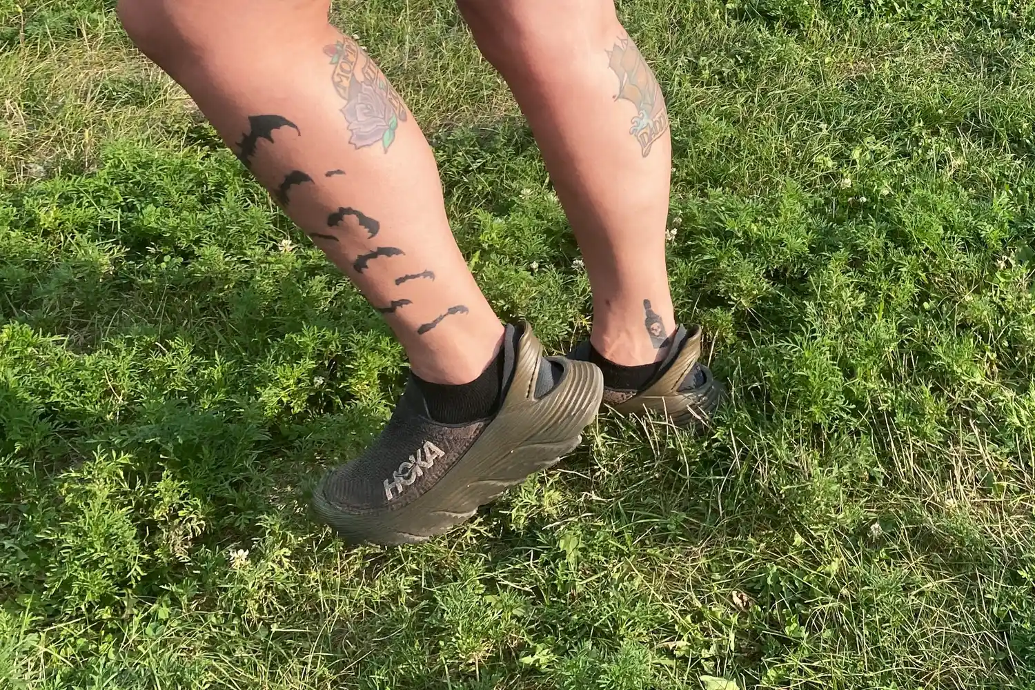 Two legs wearing Hoka Restore TC Recovery Shoes standing in grass