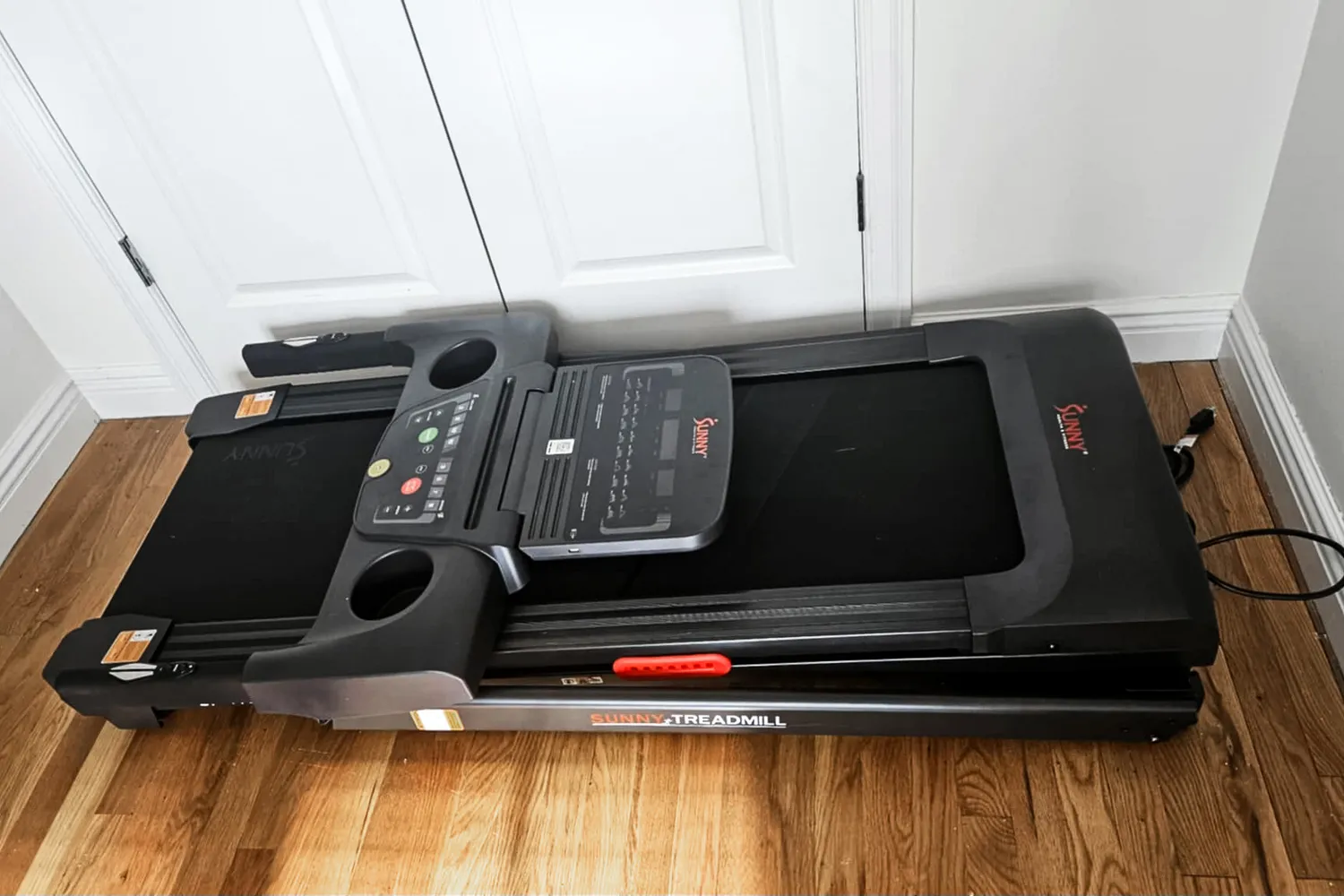 The Sunny Health & Fitness Active 400 Smart Auto Incline Wi-Fi Treadmill folded flat on a wooden floor