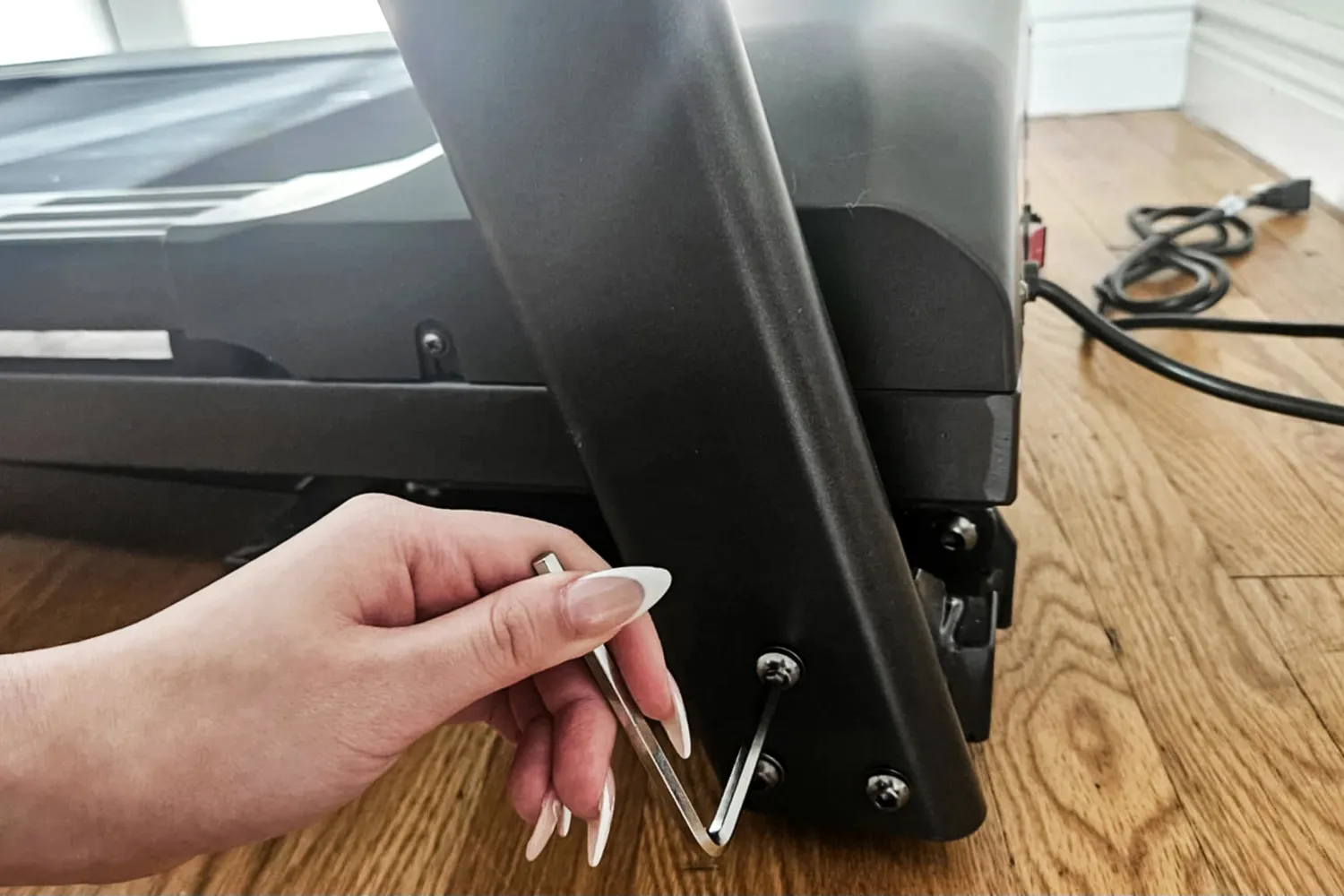 A person tightens the screws on the base of the Sunny Health & Fitness Active 400 Smart Auto Incline Wi-Fi Treadmill