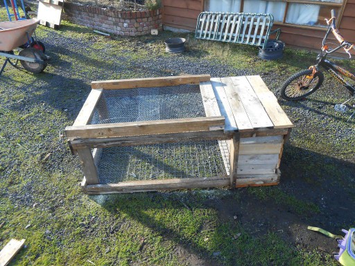 A small rabbit hutch in a yard near a bicycle.