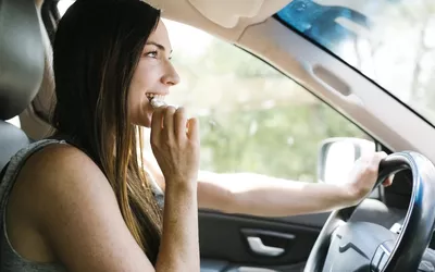 Smiling woman driving car and eating pretzel