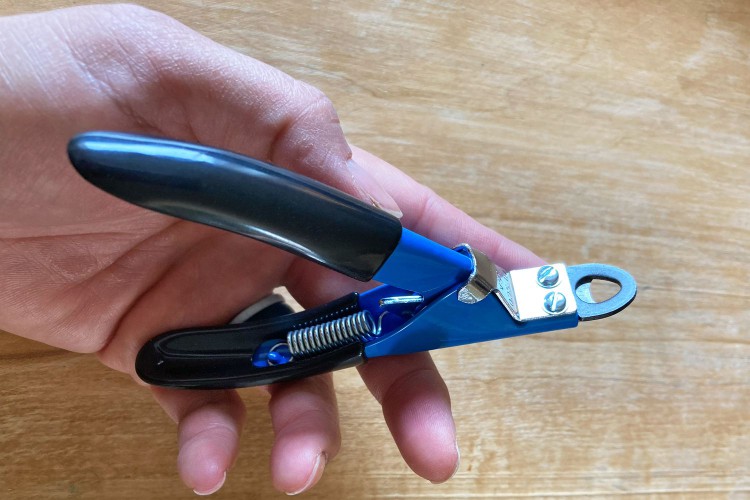 Hand holding the Resco Deluxe Pet Nail Clippers over a wooden surface