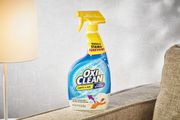 OxiClean Carpet & Area Rug Stain Remover displayed on the arm of a couch next to a lamp