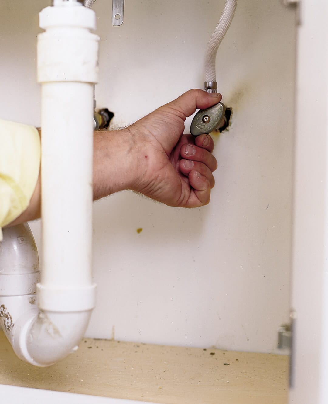 Hands shutting off water valves under kitchen sink before faucet repair.