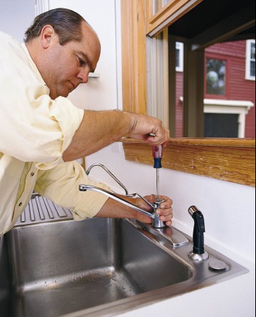 Using a screwdriver on a kitchen faucet.
