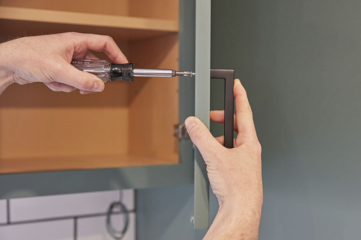 Black handle installed on mint green cabinet door with screwdriver