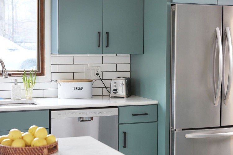 Stainless steel refrigerator and dishwasher appliances surrounded by mint green cabinets