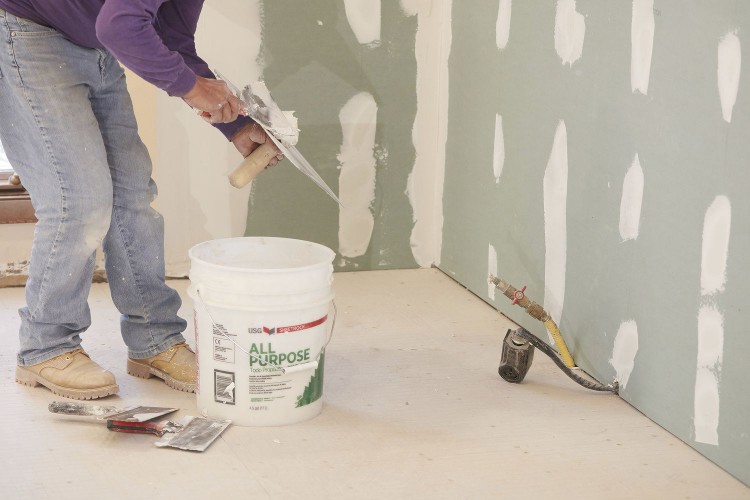 Plaster spots on wall with contractor adding more near white bucket
