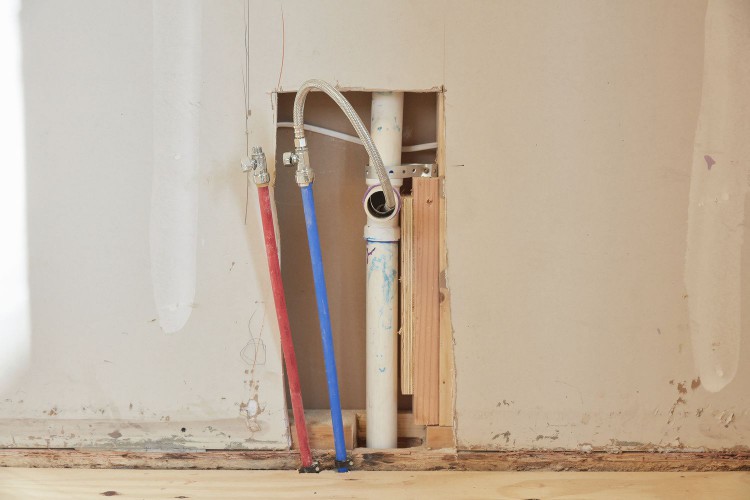 Exposed wall with plumbing pipe and blue and red wires 
