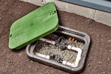 Green valve box for lawn sprinkler system buried in ground with lid removed