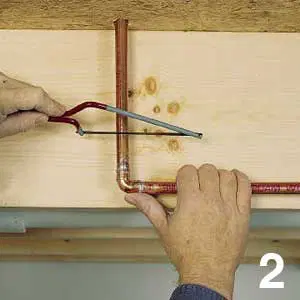 Using a hacksaw to cut a cold-water pipe.