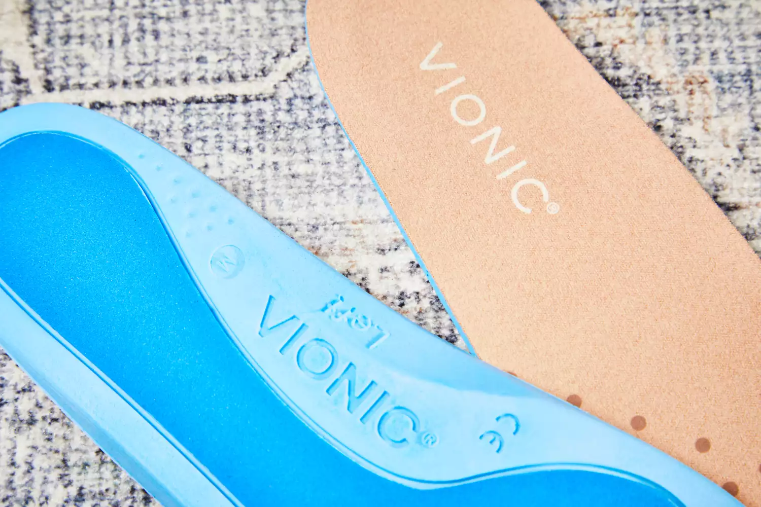 Both sides of Vionic Slimfit Orthotic Insoles displayed on a rug