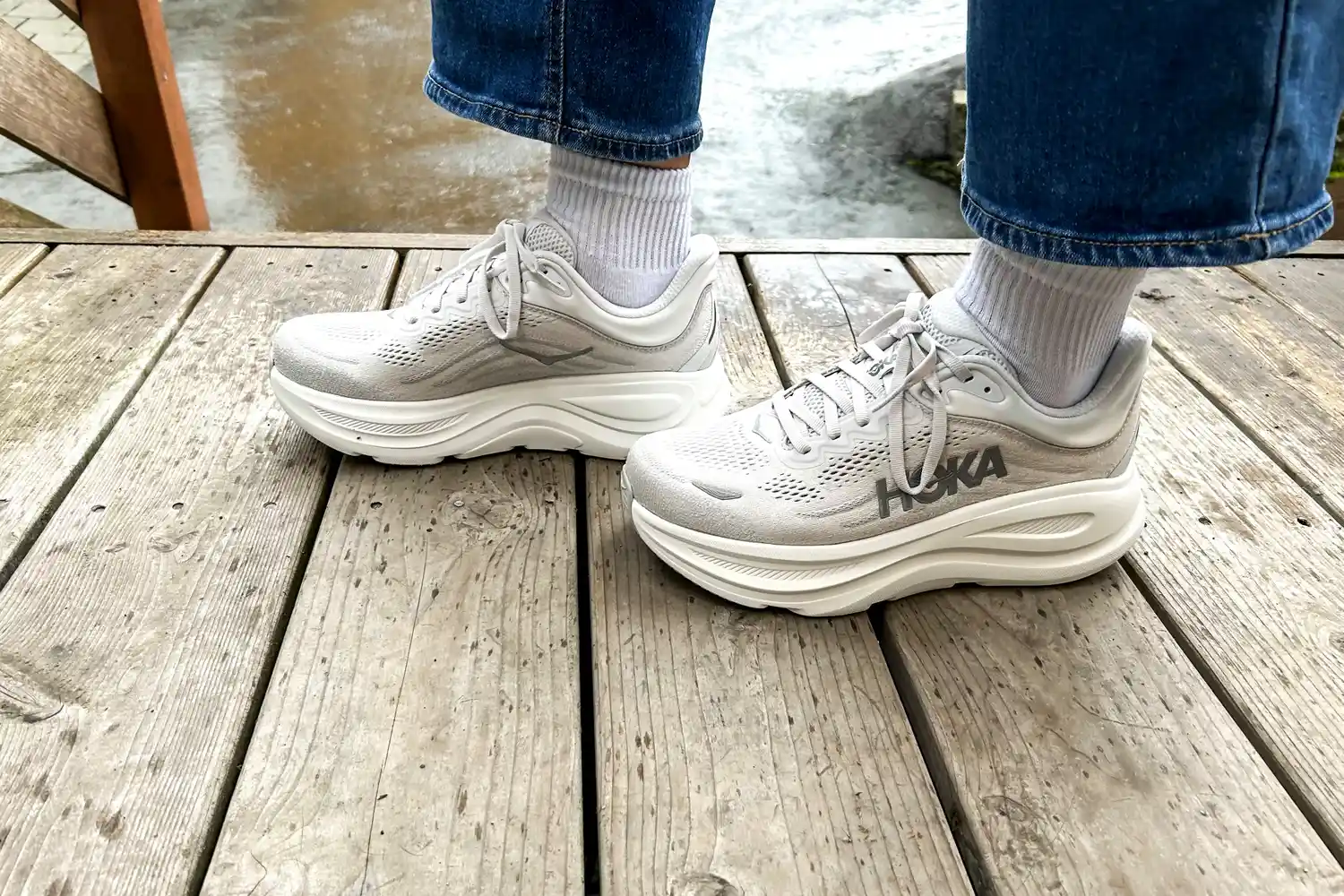 A close-up side-view of a person wearing the Hoka Bondi 9 sneakers on a wooden bridge