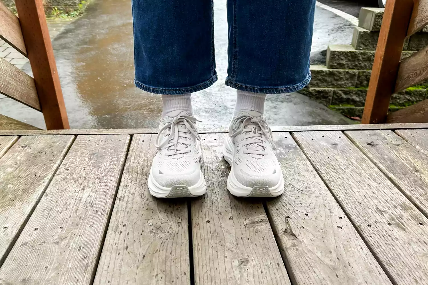 A close-up of a person's feet wearing the Hoka Bondi 9 shoes on a wooden bridge