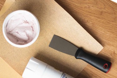 Tub with putty next to putty knife on sandpaper