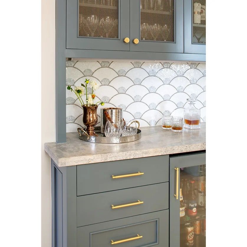 A blue-grey and white kitchen with a scalloped tile backsplash and gold hardware details