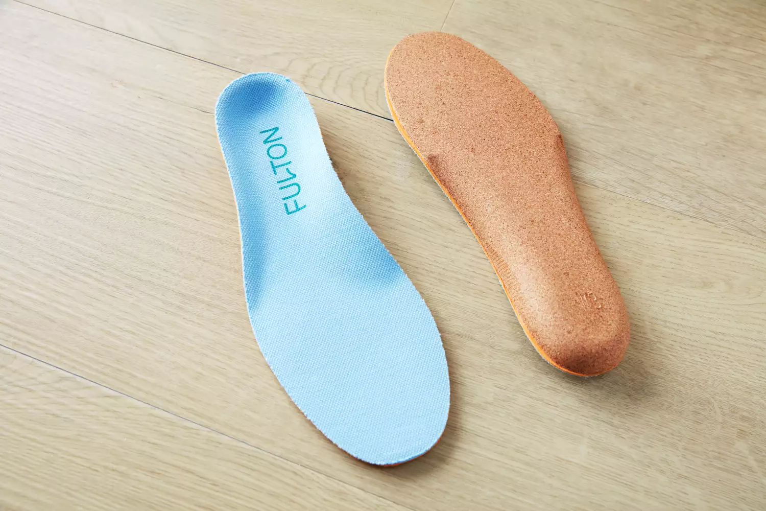 Top and bottom of Fulton Athletic Insoles displayed on a wood floor