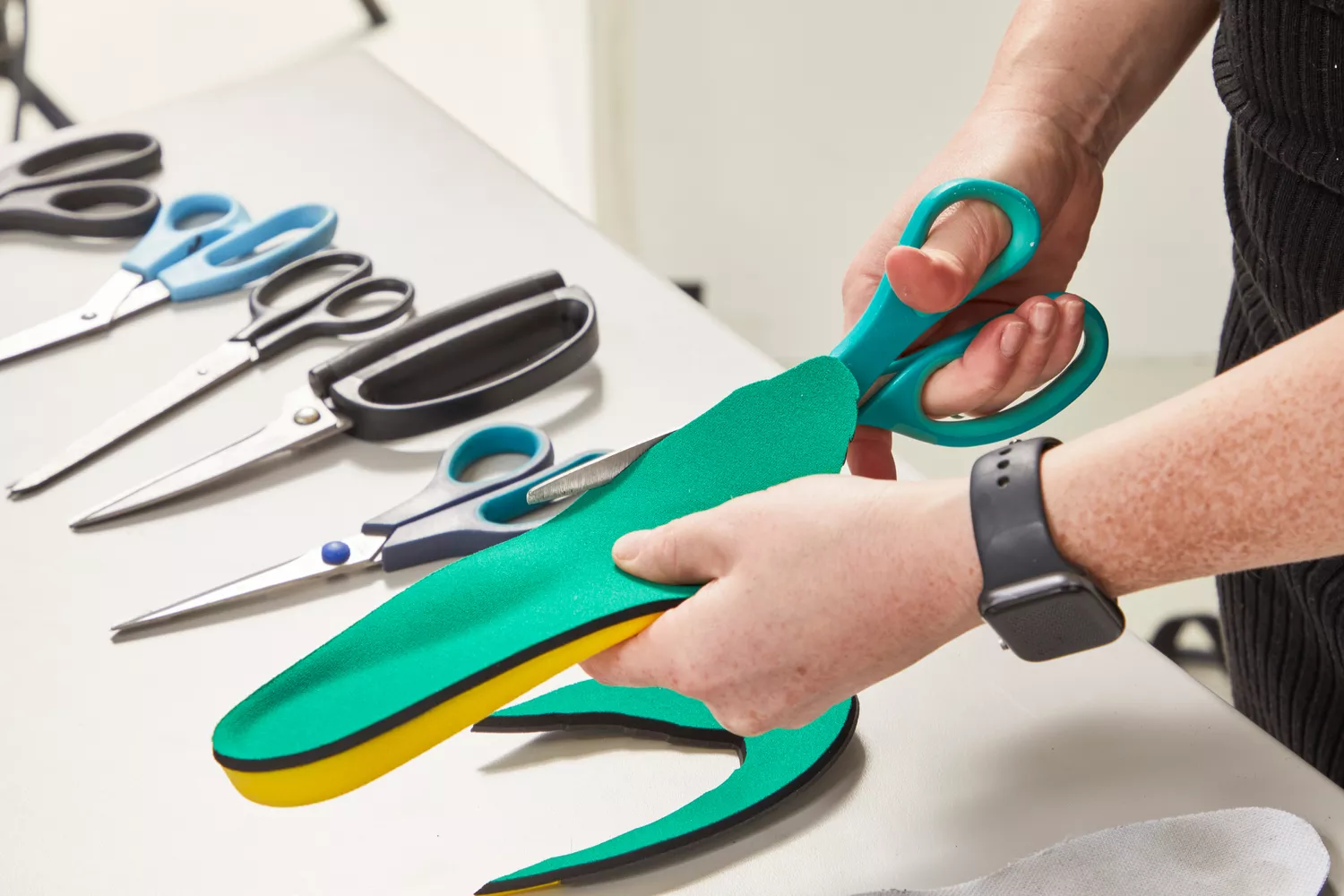 Hands trimming a Spenco PolySorb Cross Trainer Insole with scissors