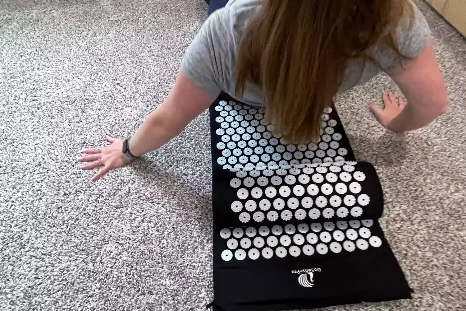 Back view of woman lowering her back down onto the DoSensePro Acupressure Mat and Pillow Set