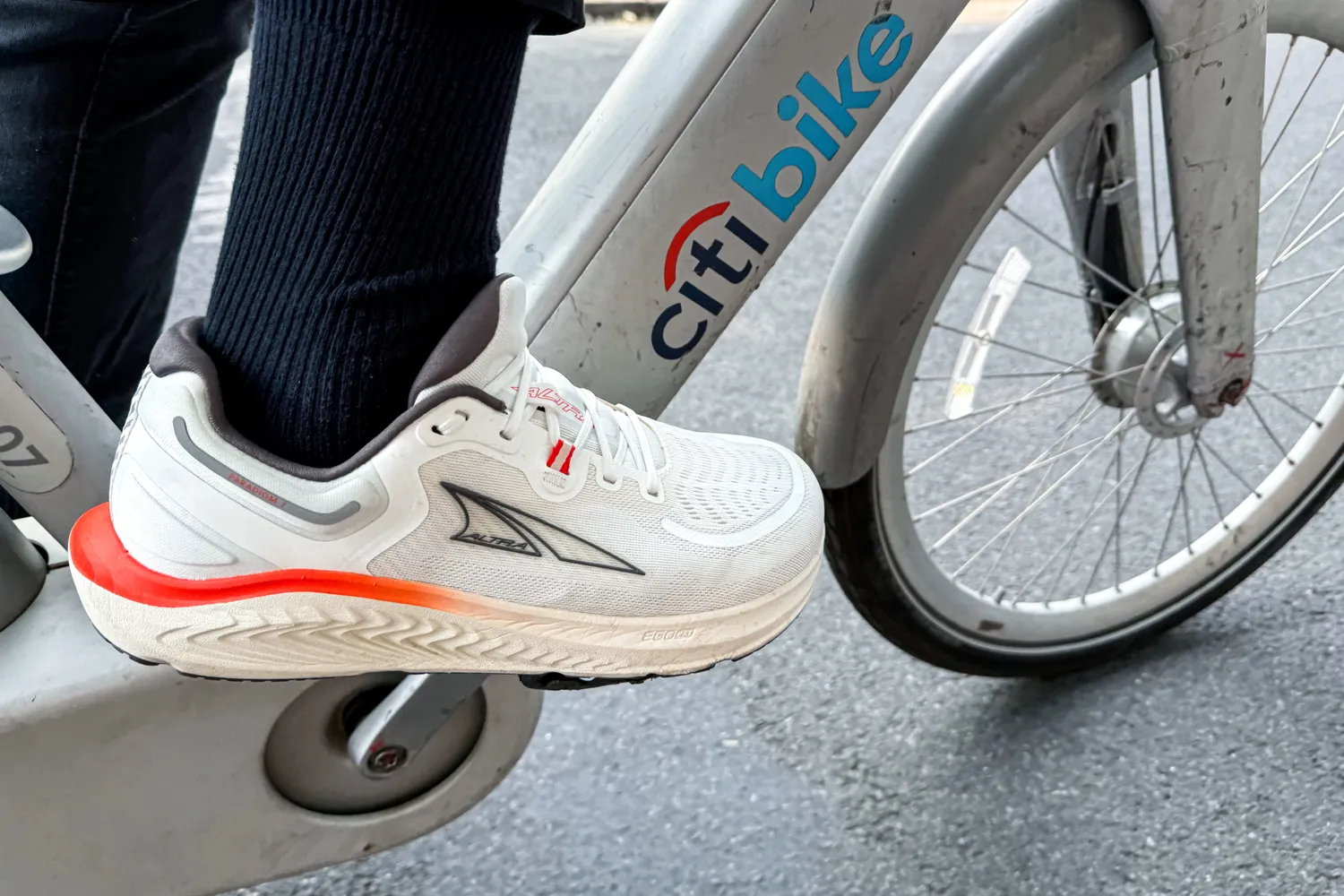 A person pedals a bicycle wearing the Altra Men's Paradigm 7 Sneakers