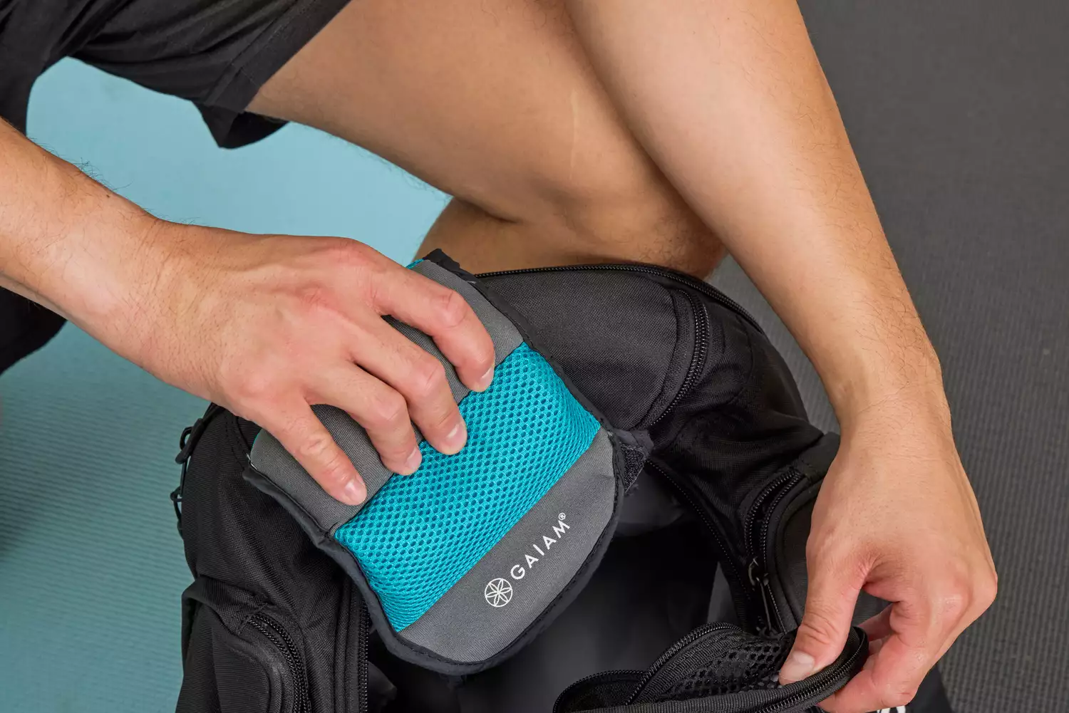 A person places a Gaiam Fitness Ankle Weight into a backpack
