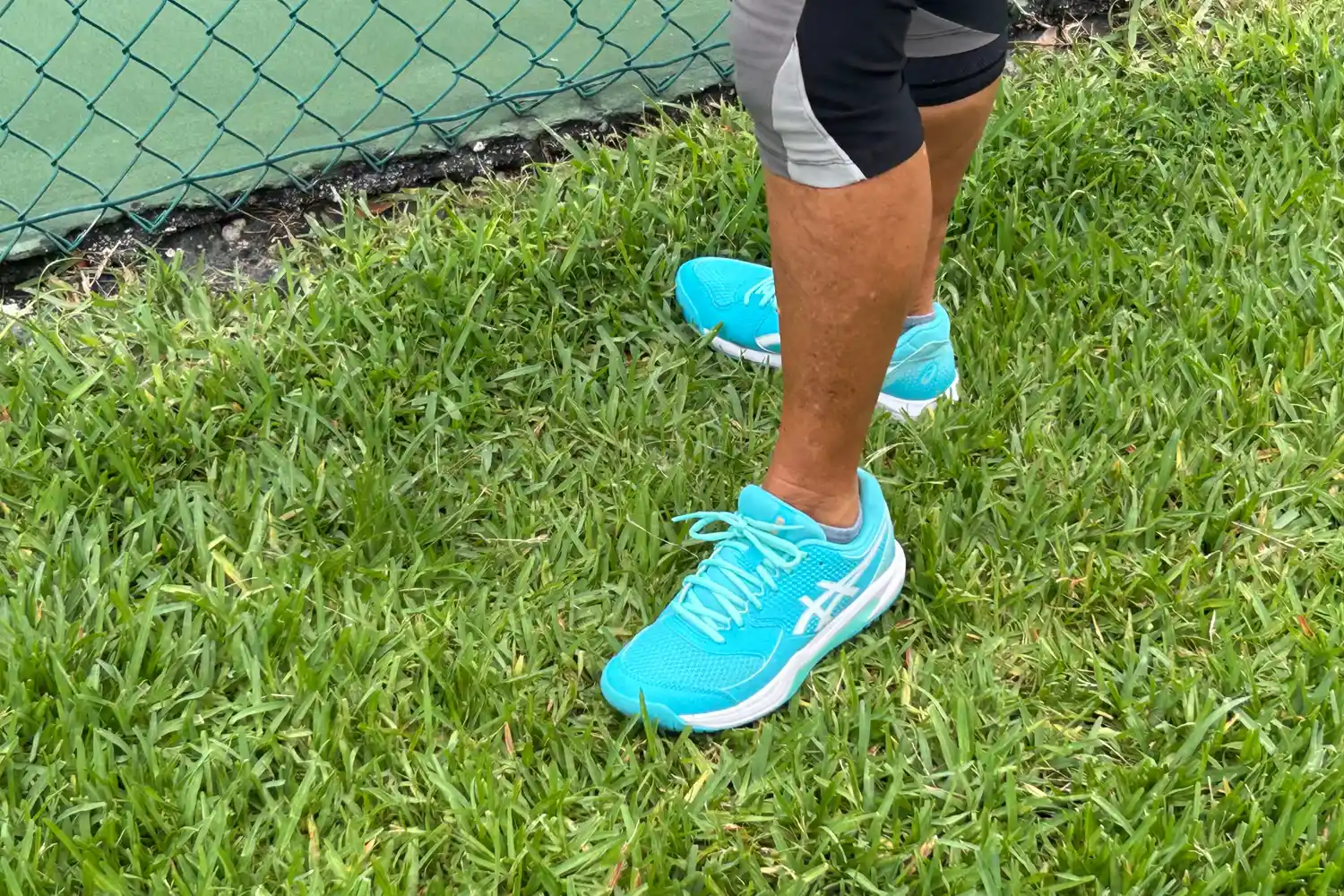 A person wears the Asics Women's Gel-Dedicate 8 Pickleball Shoes while standing in grass