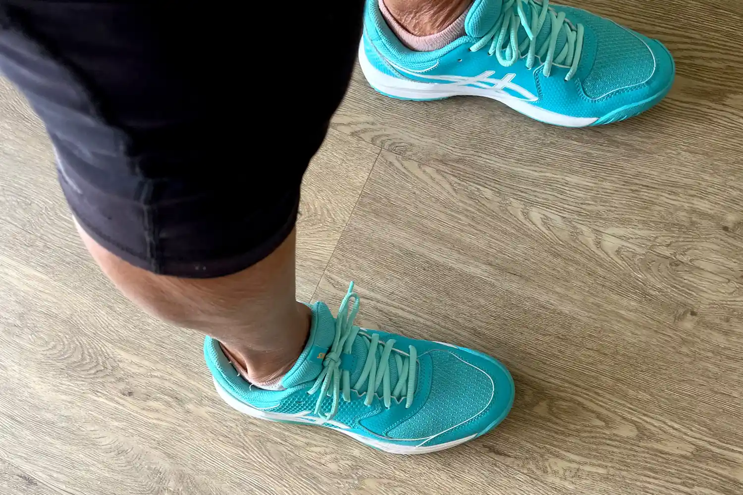 A person wears the Asics Women's Gel-Dedicate 8 Pickleball Shoes on a wooden floor