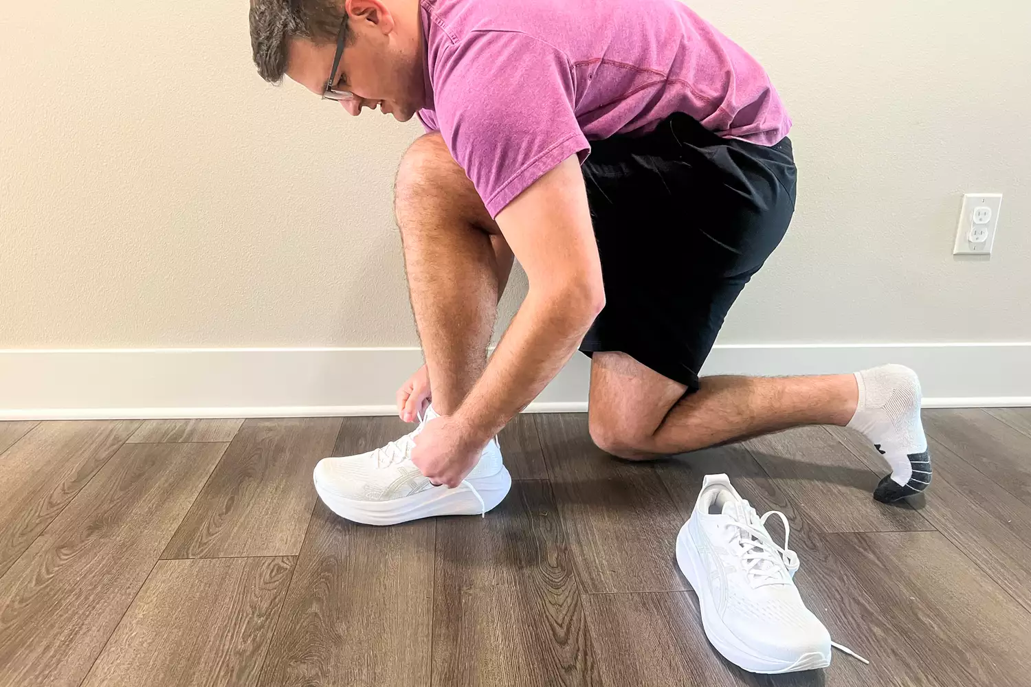 A person kneeling while tying a Asics Men's GEL-NIMBUS 27 sneaker