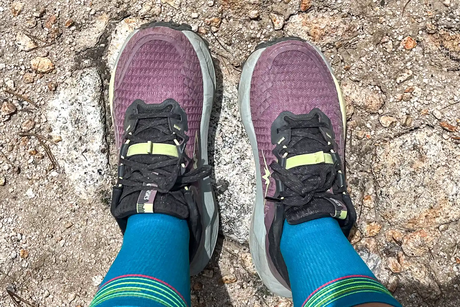 A person wearing Asics Women's Gel-Trabuco 13 Trail Running Sneakers and blue socks standing on rocky terrain