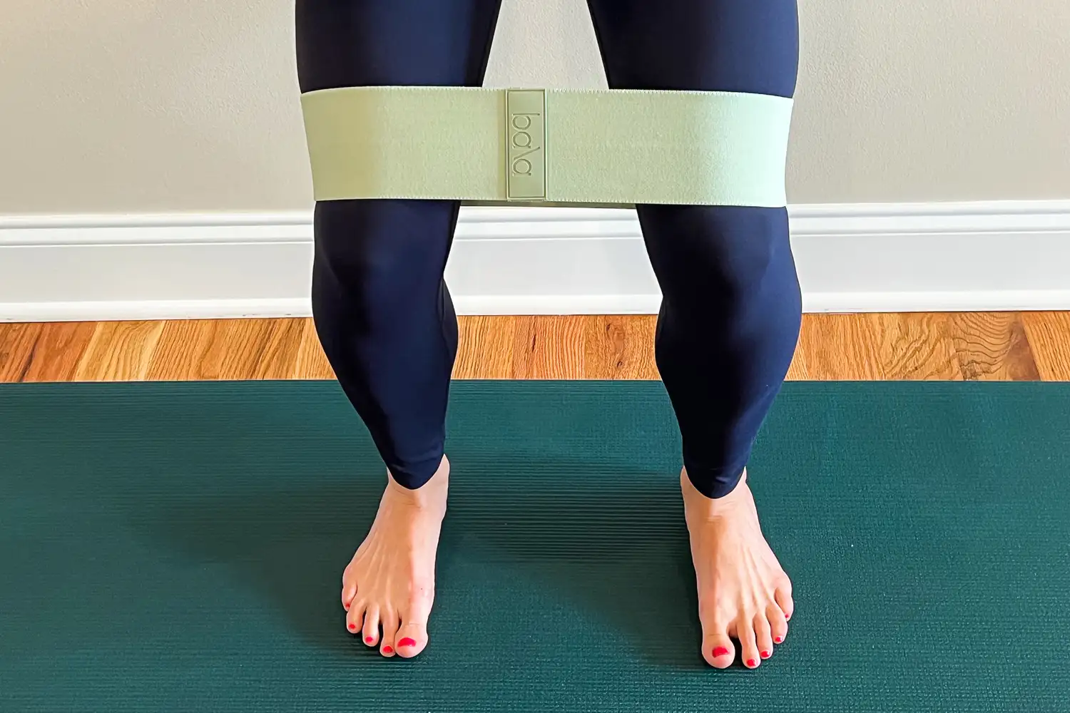 A person standing on a mat with a Bala Band around their thighs viewed from the knees to the feet