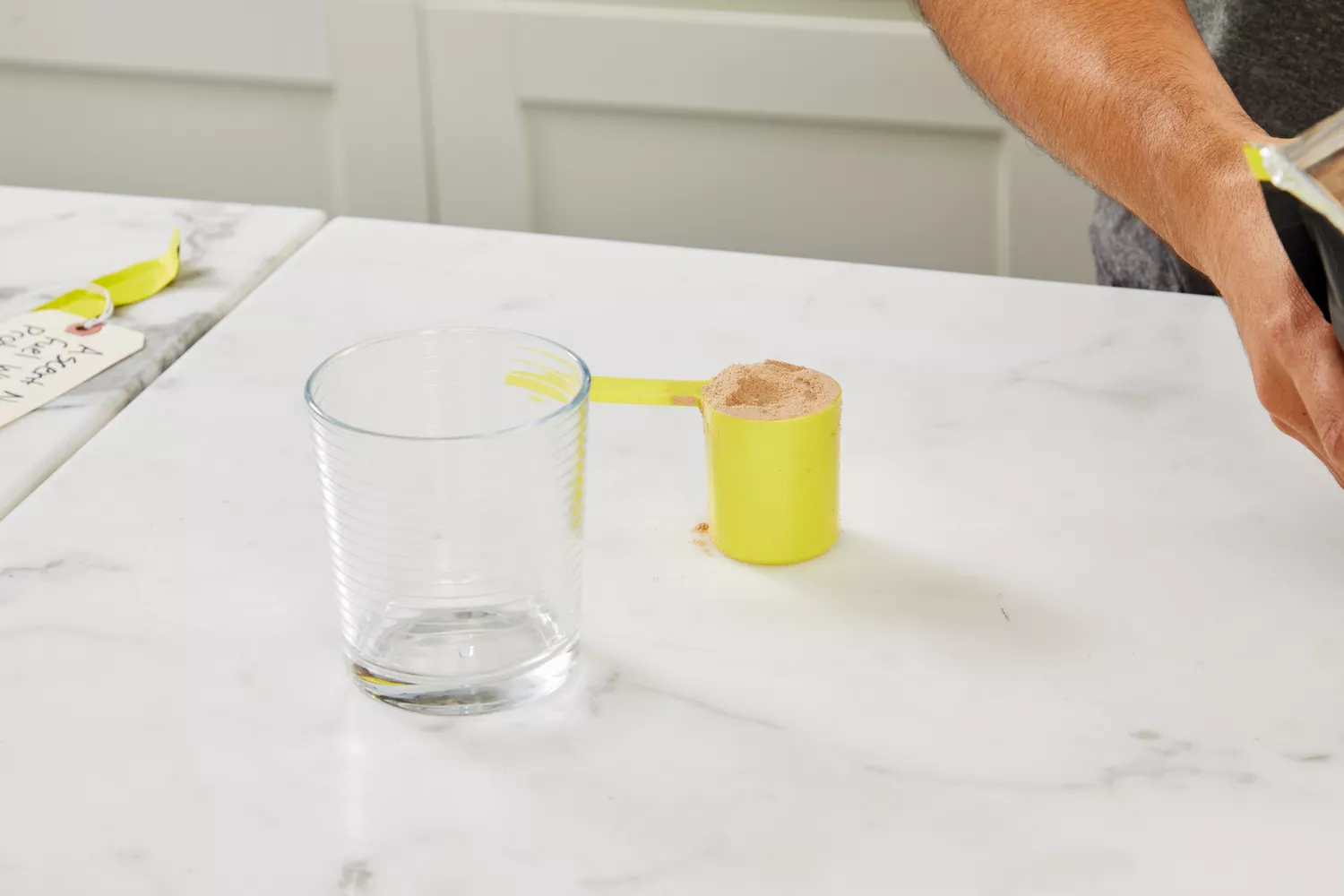 Scoop of Ascent Native Fuel Whey Protein Powder displayed next to a glass on a marble counter