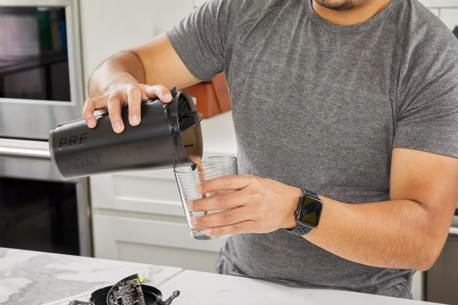 Hands pouring a protein drink from a blender bottle into a glass