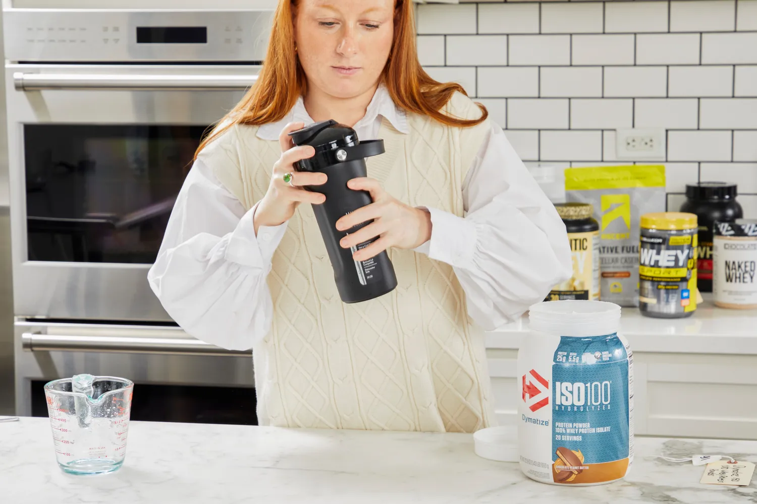 Person shaking a blender bottle with Dymatize ISO100 Whey Protein Powder Chocolate Peanut Butter on counter