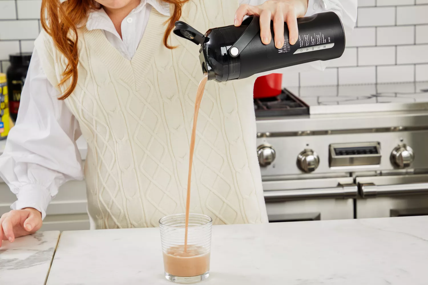 Hand pouring a protein drink into a glass from a blender bottle