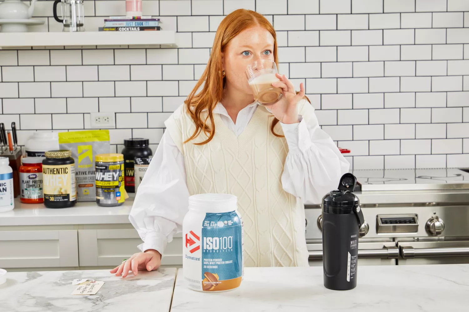 A person drinking a protein shake with Dymatize ISO100 Whey Protein Powder Chocolate Peanut Butter on counter