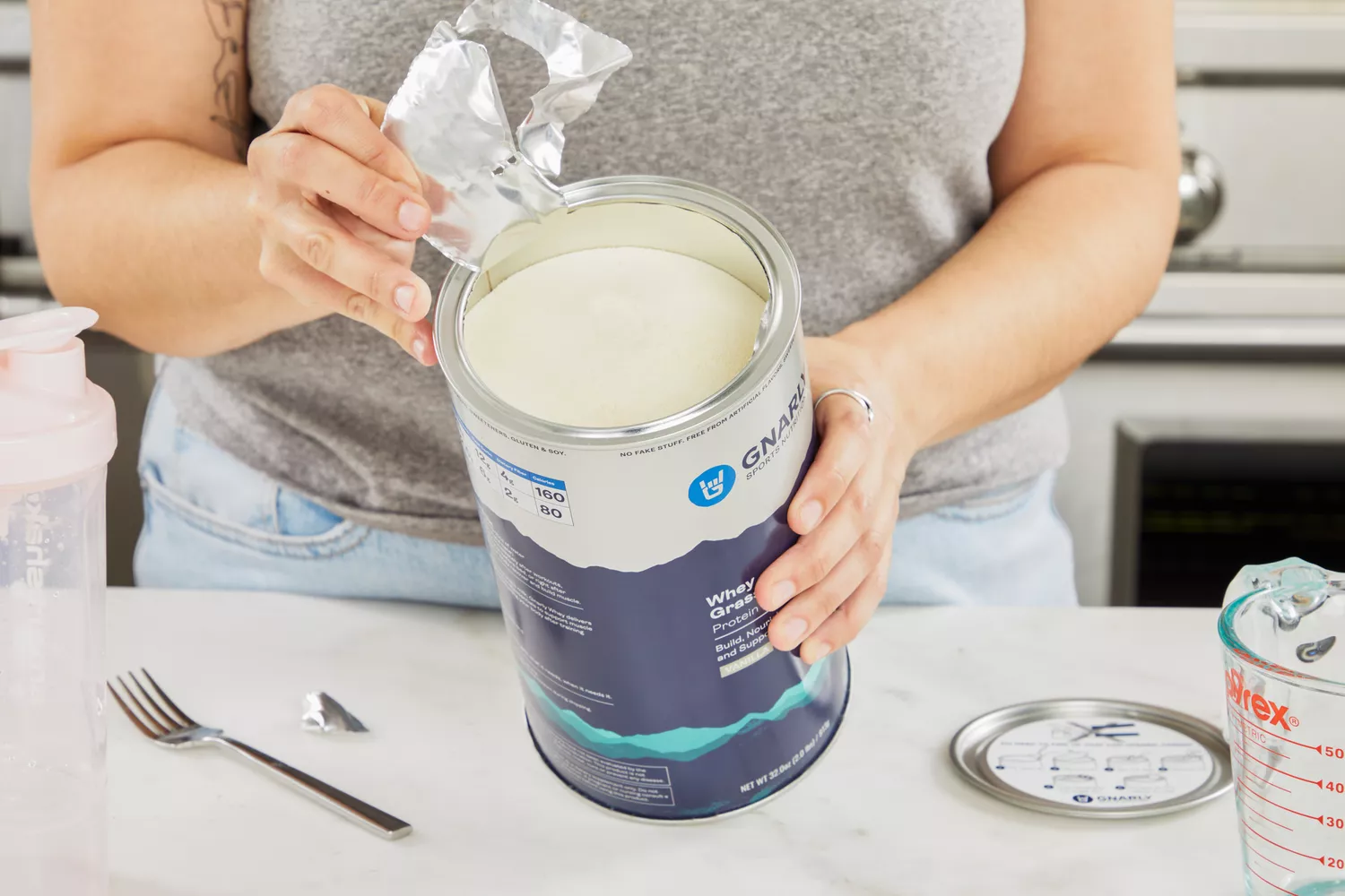 Hand pulling foil off a can of Gnarly Grass-Fed Whey Vanilla Protein Supplement