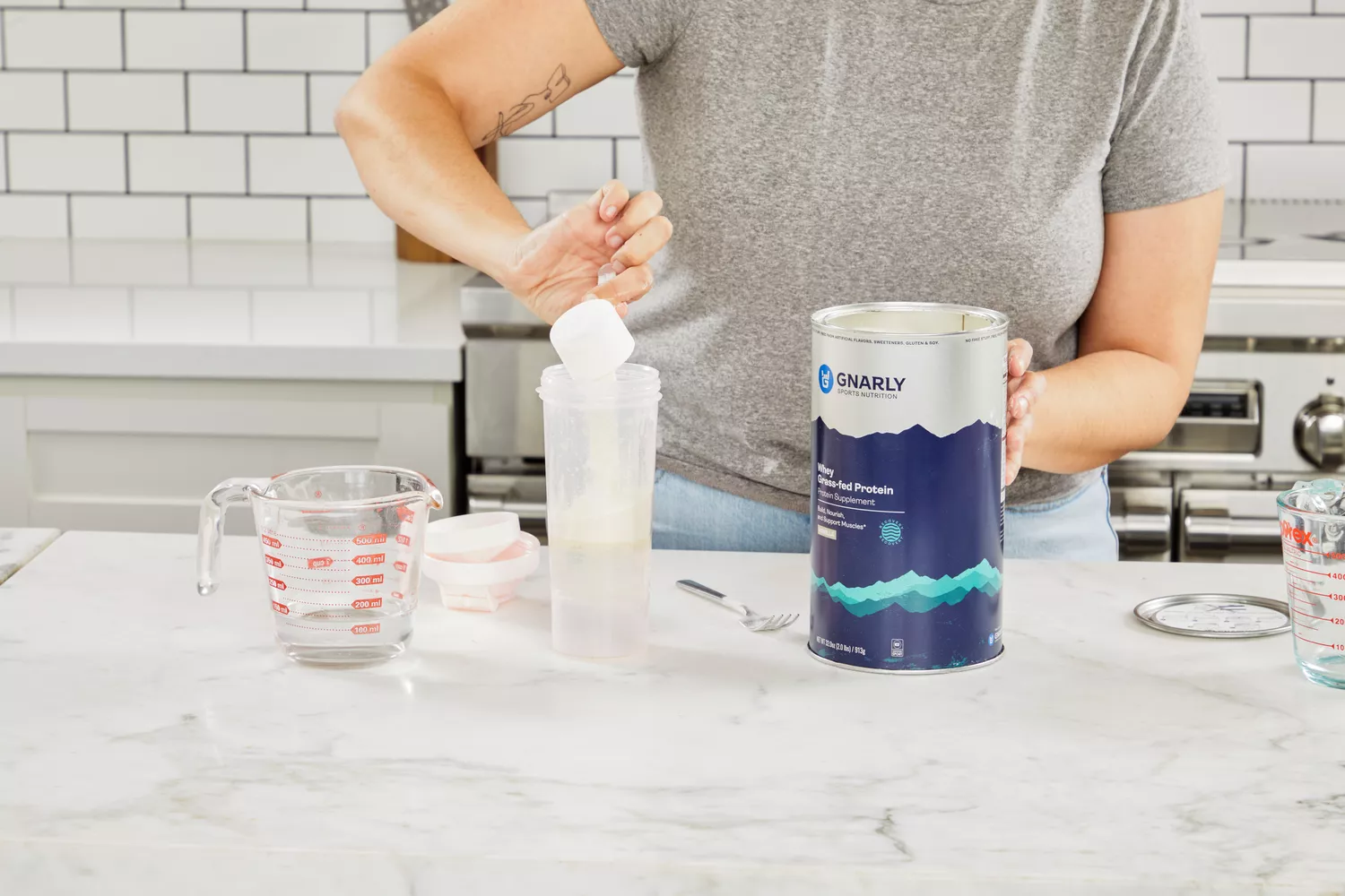 Hand pouring a scoop of Gnarly Grass-Fed Whey Vanilla Protein Supplement into a shaker bottle