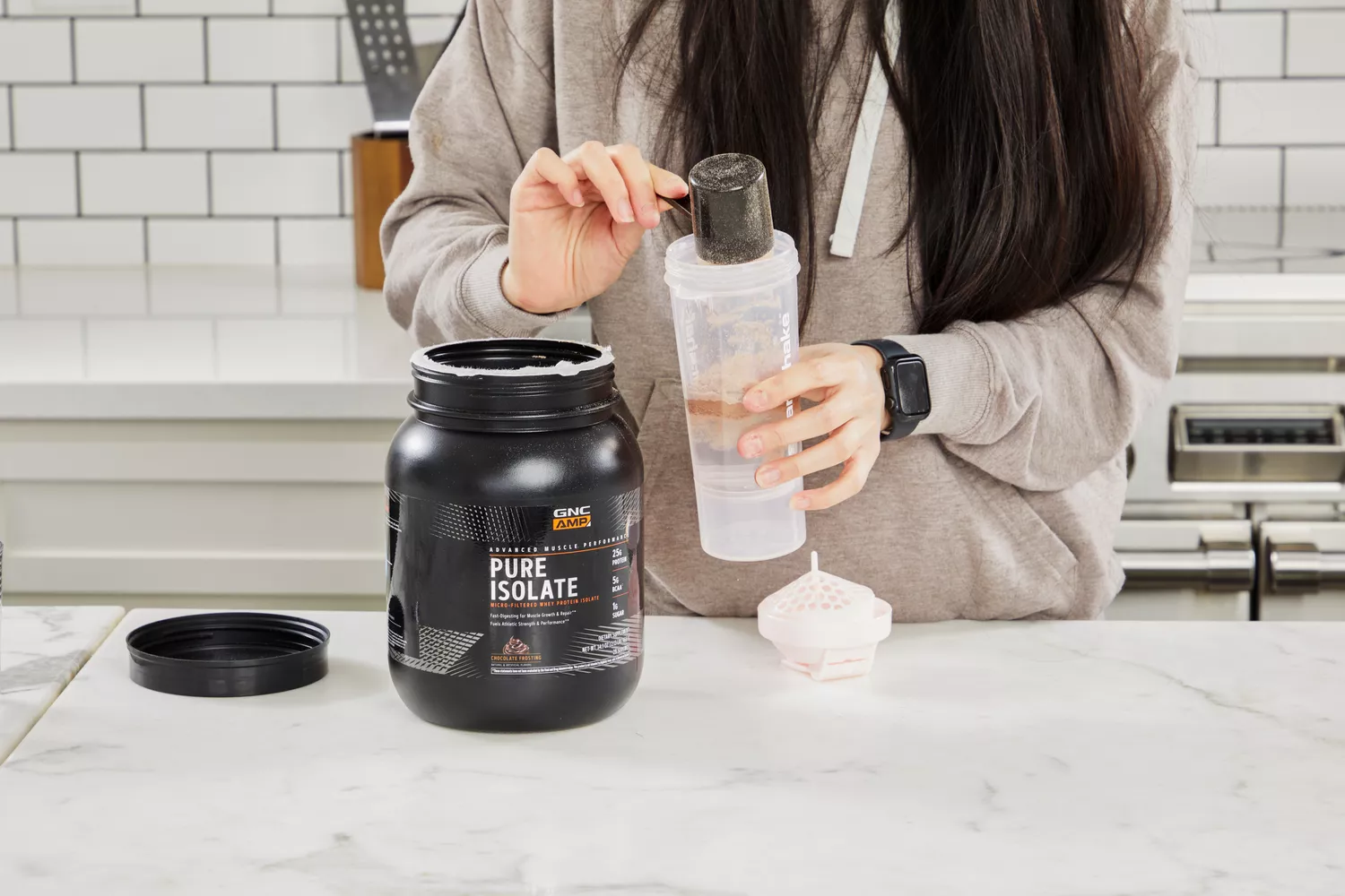 Hands scooping GNC AMP Pure Isolate Whey Protein powder into a shaker bottle