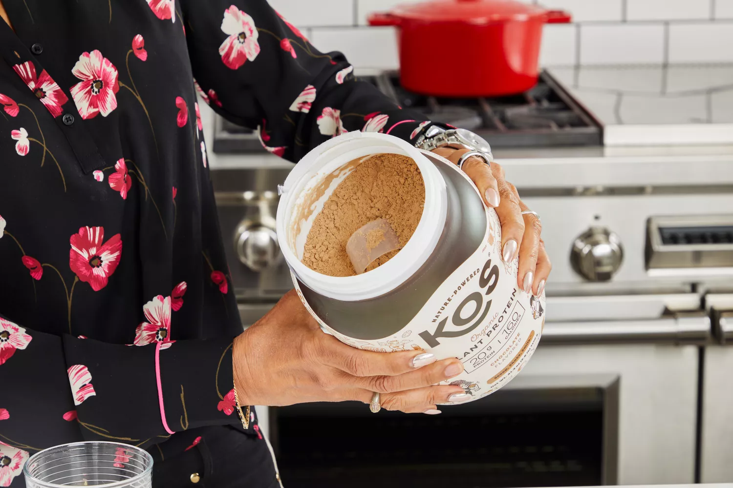 Hands holding an open container of KOS Vegan Superfood Protein Powder