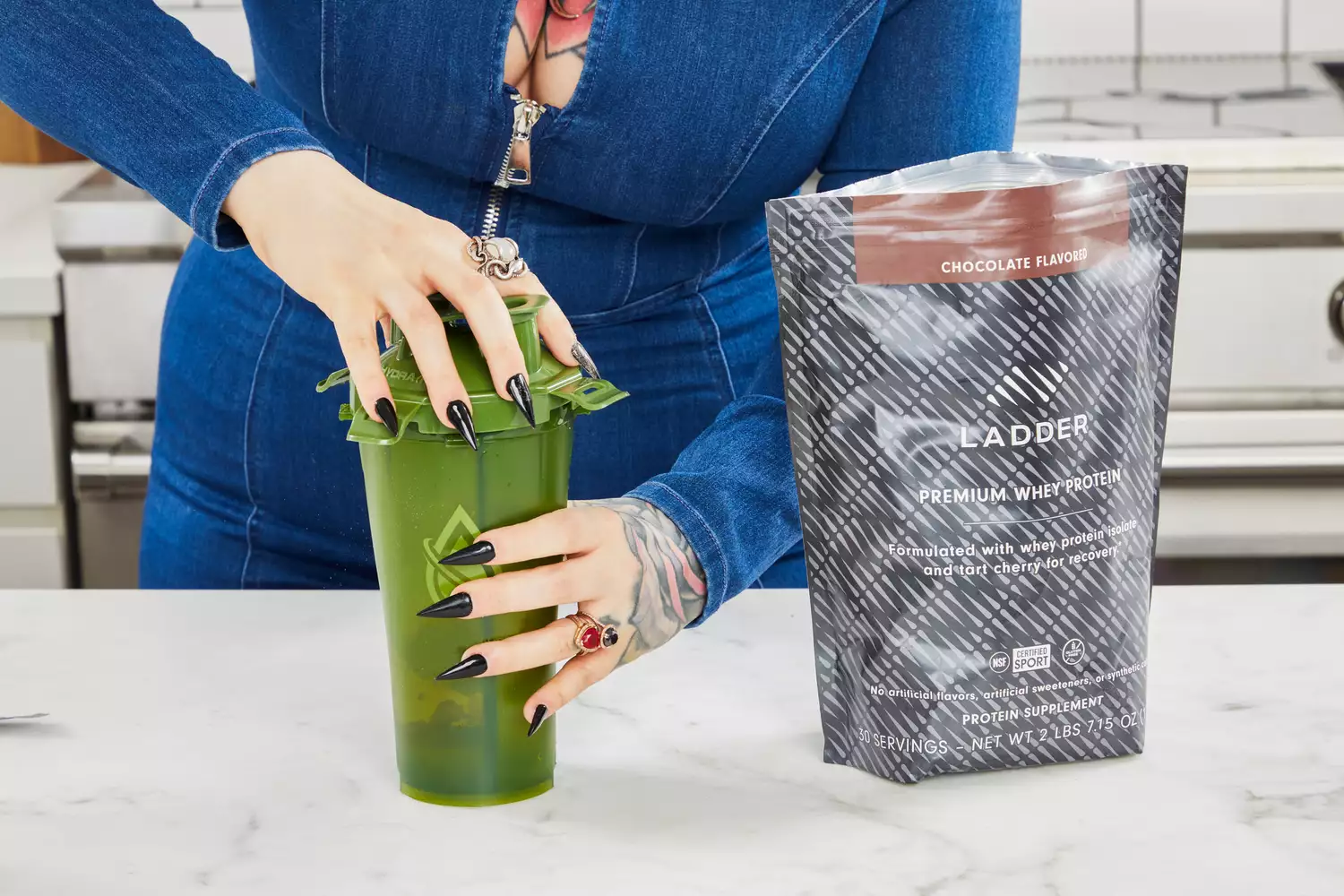 Hands putting a lid on a shaker bottle next to pouch of Ladder Whey Protein Powder