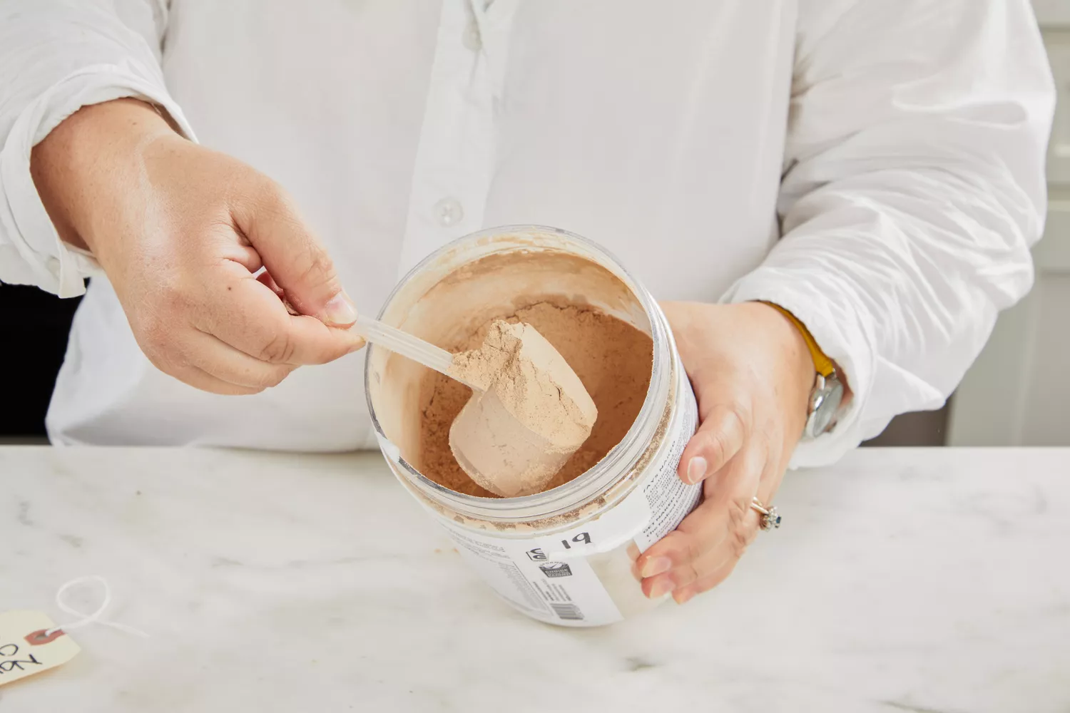Hand scooping Naked Whey Chocolate Protein Powder from the container
