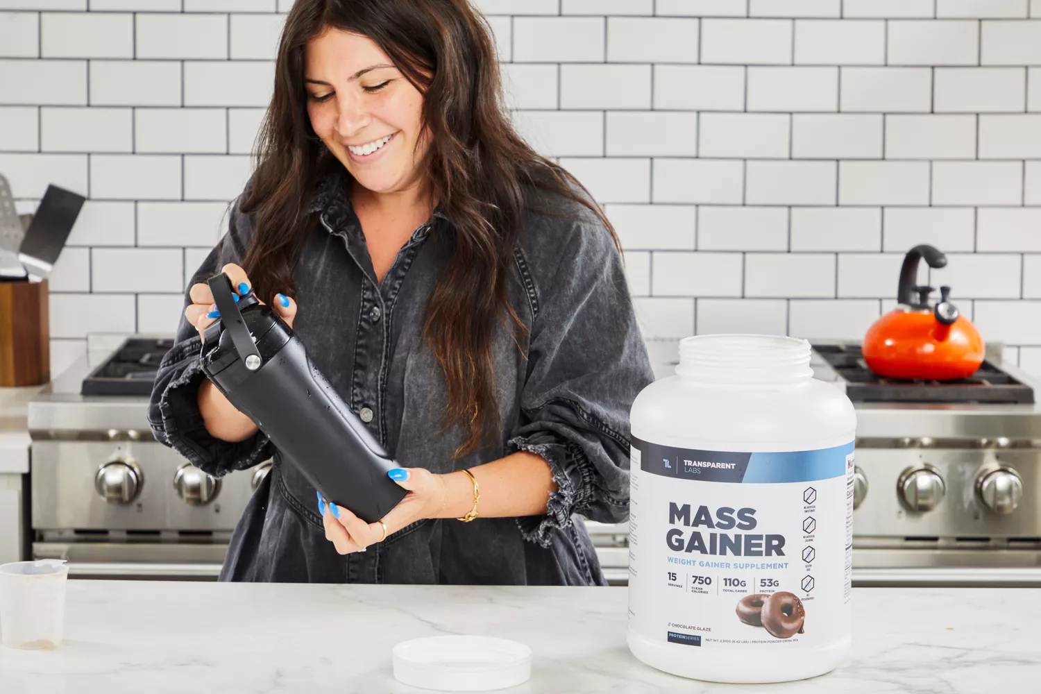 A person holding a shaker bottle next to container of Transparent Labs Mass Gainer Weight Gainer Supplement