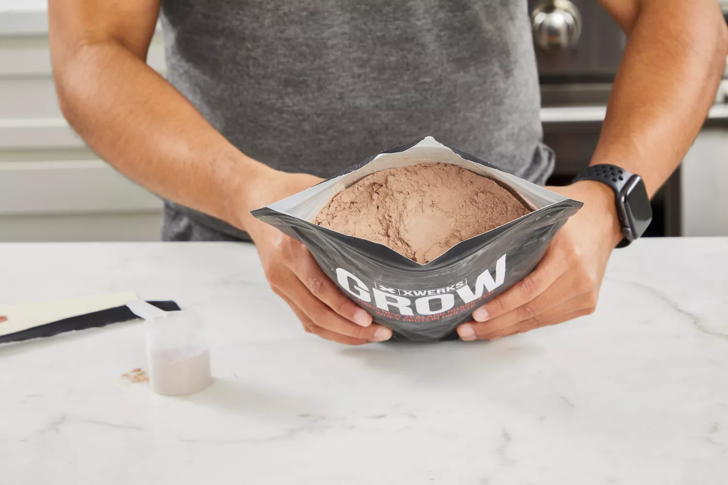 Hands holding an open bag of Xwerks Grow 100% New Zealand Grass-Fed Whey Protein Isolate powder