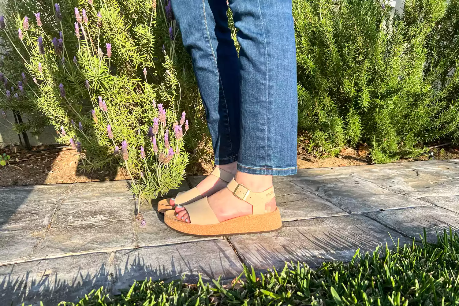 A close-up of legs posed to the side on stones while wearing the Birkenstock Women's Glenda