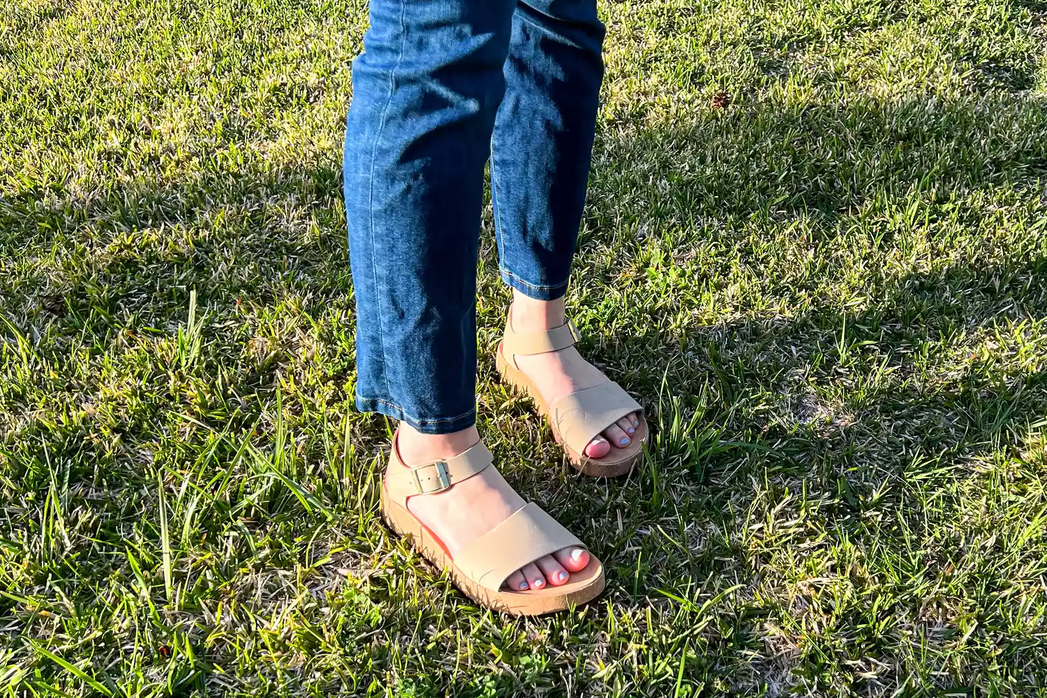 A close-up of a person's legs posed while wearing Birkenstock Women's Glenda on grass